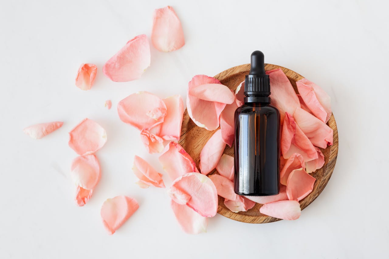 services-04 Top view of empty brown bottle for skin care product placed on wooden plate with fresh pink rose petals on white background isolated